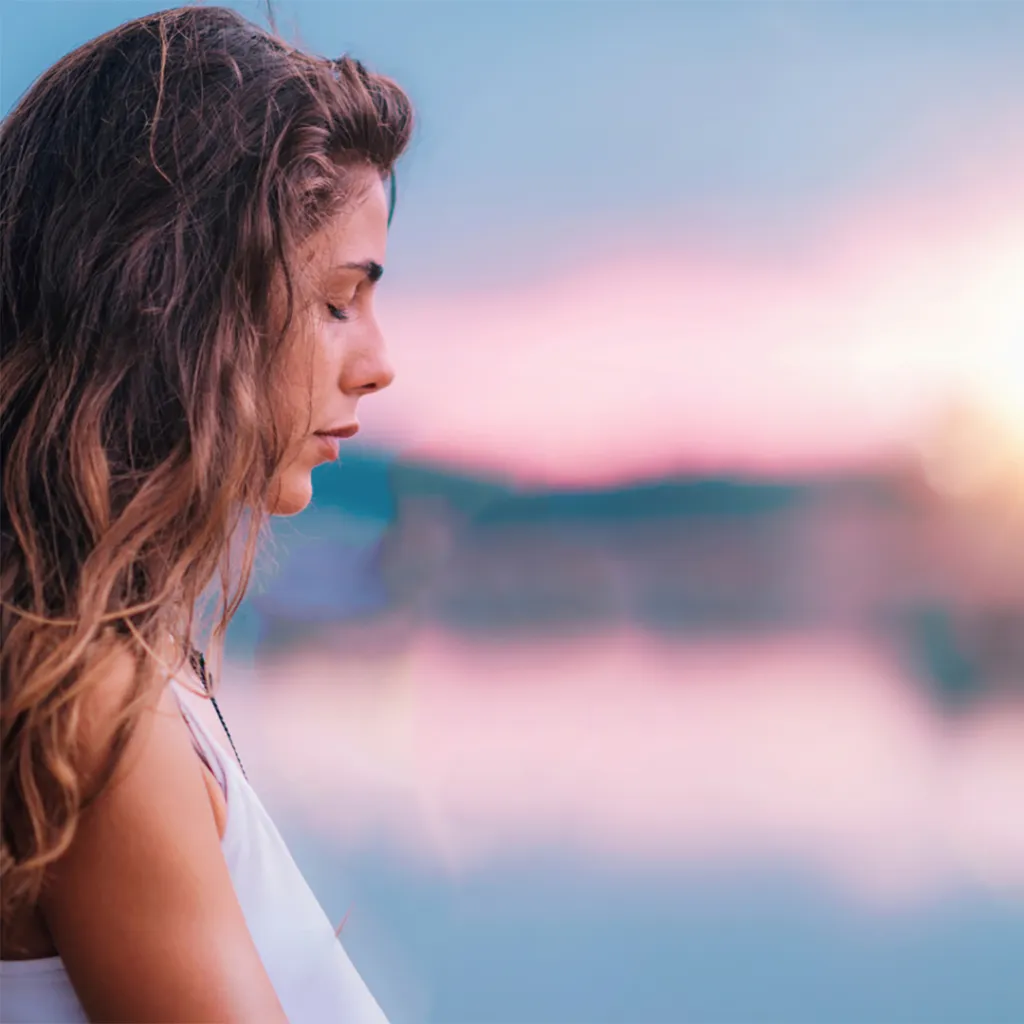 Nainen meditoimassa auringonlaskussa